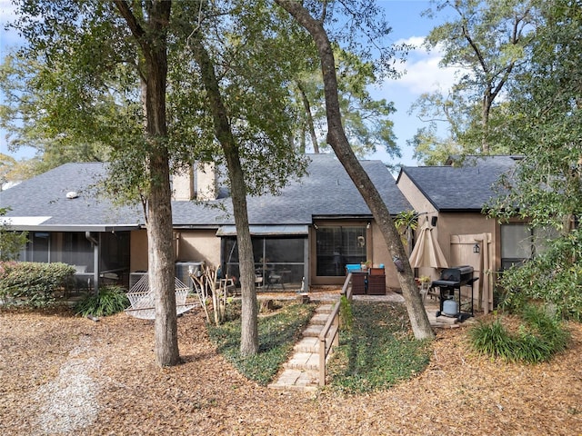 back of property with a sunroom, roof with shingles, and stucco siding