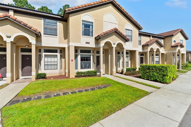 mediterranean / spanish-style home with stucco siding, a front lawn, and a tile roof