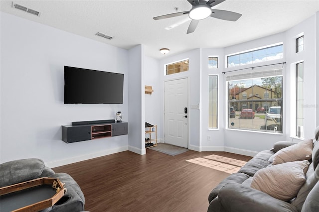 living room featuring dark wood-type flooring, baseboards, visible vents, and a textured ceiling