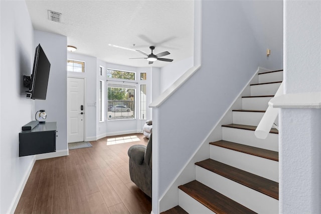 staircase with visible vents, a textured ceiling, wood finished floors, baseboards, and ceiling fan