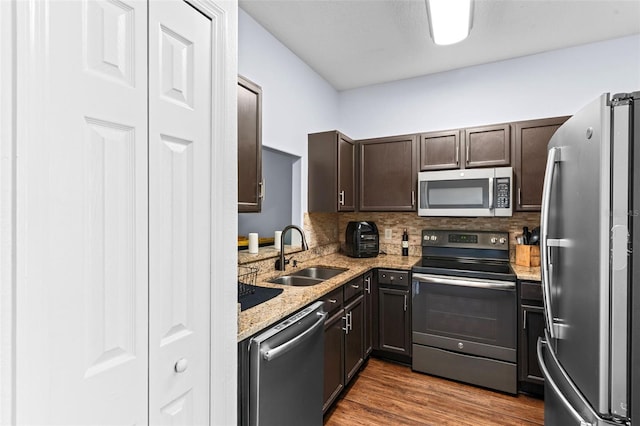 kitchen with tasteful backsplash, dark brown cabinetry, wood finished floors, stainless steel appliances, and a sink