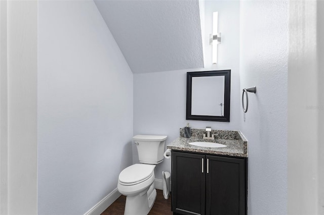 half bath featuring toilet, wood finished floors, baseboards, vanity, and vaulted ceiling