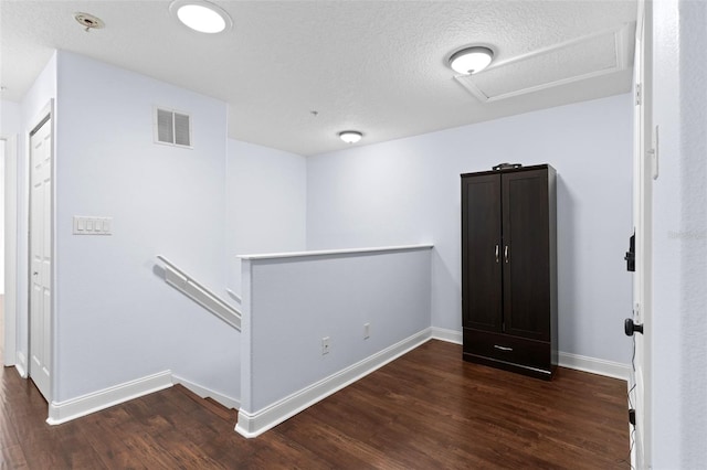 unfurnished room with attic access, baseboards, visible vents, and dark wood-style flooring