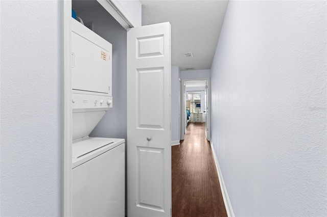 washroom with visible vents, baseboards, stacked washer and dryer, laundry area, and dark wood-style floors