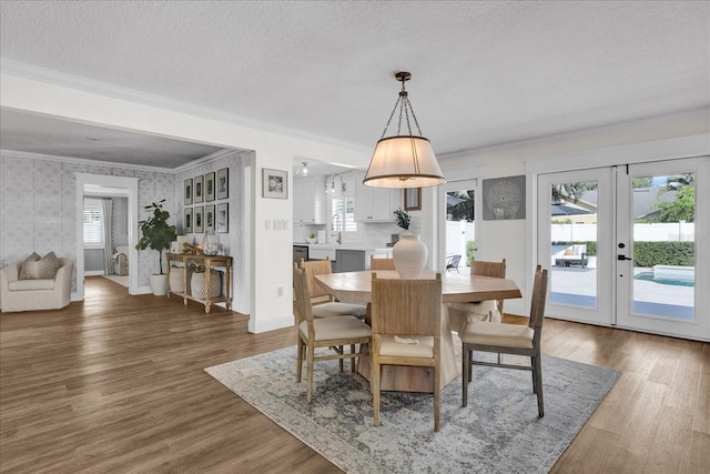 dining area featuring a textured ceiling, wood finished floors, wallpapered walls, and ornamental molding