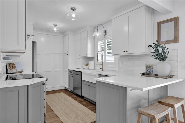 kitchen featuring a peninsula, gray cabinetry, dishwasher, black electric cooktop, and a kitchen bar