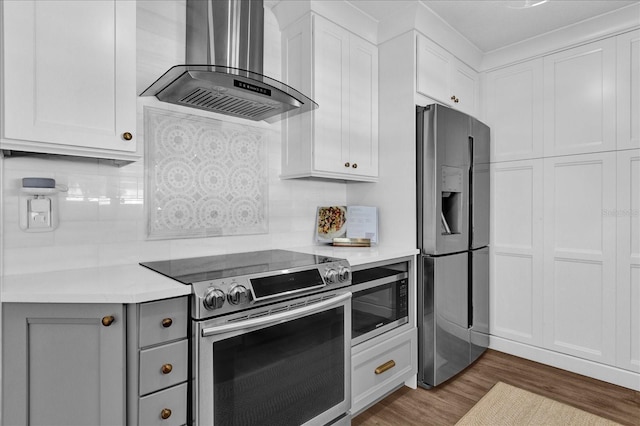 kitchen featuring wood finished floors, stainless steel appliances, light countertops, white cabinetry, and wall chimney exhaust hood