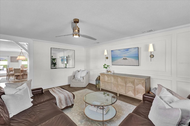 living room featuring wood finished floors, visible vents, a textured ceiling, crown molding, and a decorative wall