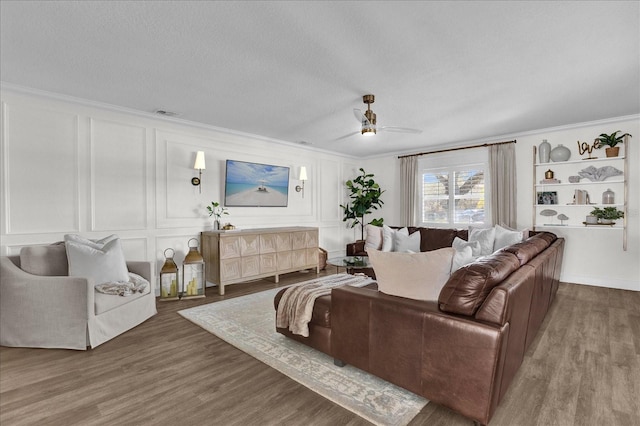 living area featuring ornamental molding, a textured ceiling, wood finished floors, a decorative wall, and ceiling fan