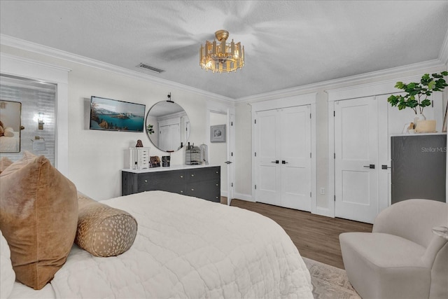 bedroom featuring visible vents, multiple closets, ornamental molding, wood finished floors, and a textured ceiling