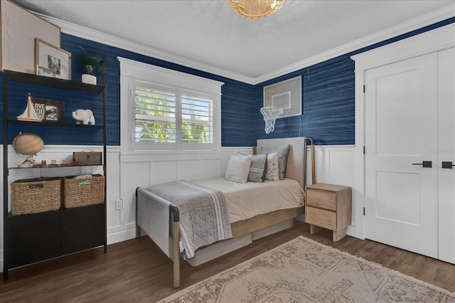 bedroom featuring wood finished floors, wainscoting, wallpapered walls, and ornamental molding