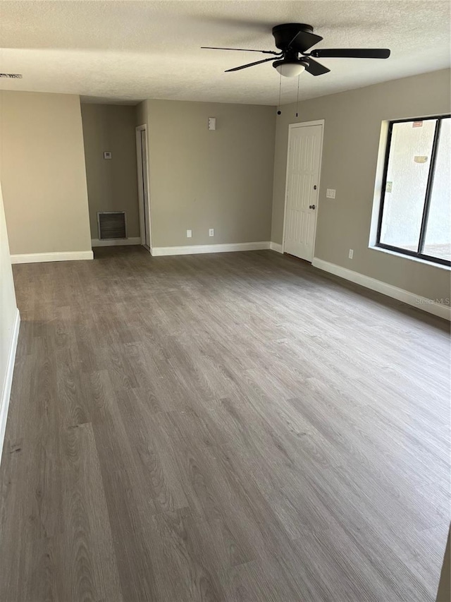 empty room featuring baseboards, a textured ceiling, visible vents, and dark wood-type flooring