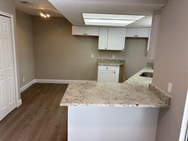 kitchen featuring a peninsula, dark wood-type flooring, a sink, white cabinets, and light stone countertops