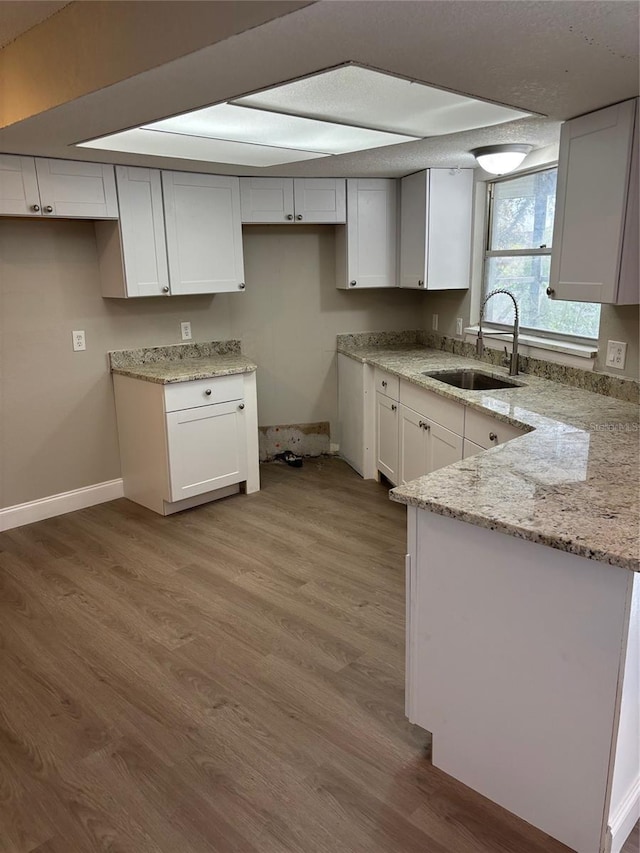 kitchen with wood finished floors, a peninsula, light stone counters, and a sink