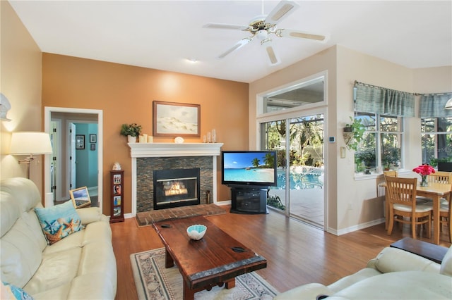 living room with a ceiling fan, a fireplace, baseboards, and wood finished floors