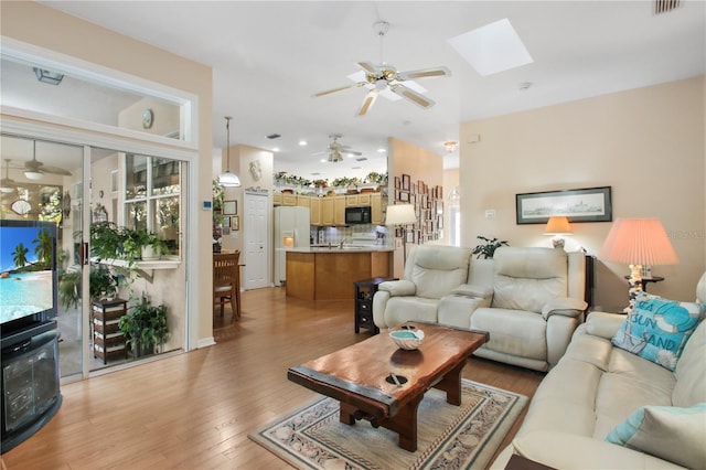 living area with light wood-style floors, a skylight, and ceiling fan