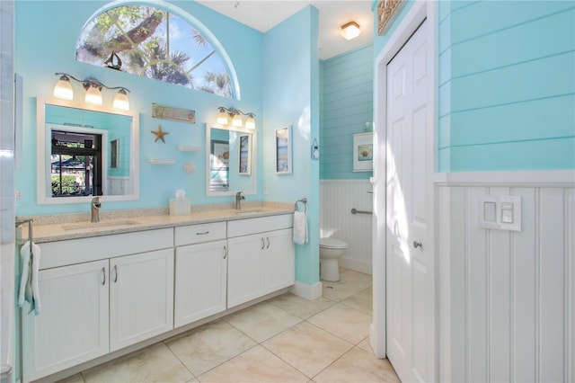 bathroom featuring a wainscoted wall, tile patterned flooring, a sink, and toilet