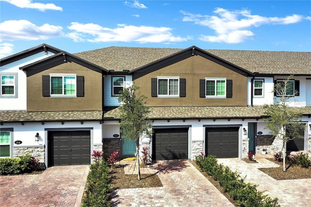 townhome / multi-family property with driveway, stone siding, an attached garage, and stucco siding