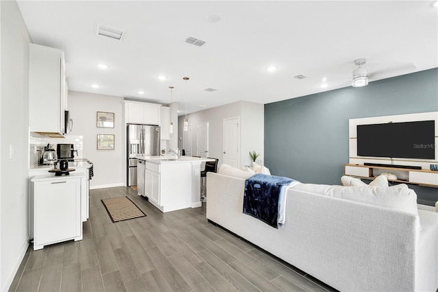 kitchen with stainless steel appliances, light countertops, visible vents, open floor plan, and wood finished floors