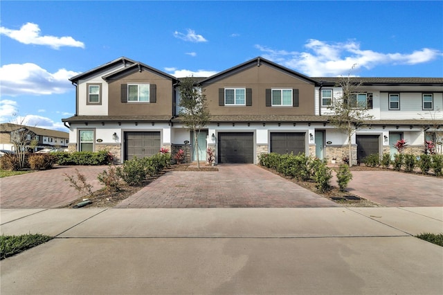 townhome / multi-family property with stone siding, driveway, an attached garage, and stucco siding