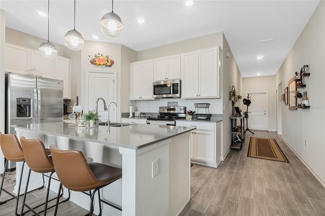 kitchen featuring stainless steel appliances, light wood-style floors, white cabinetry, a sink, and a kitchen bar