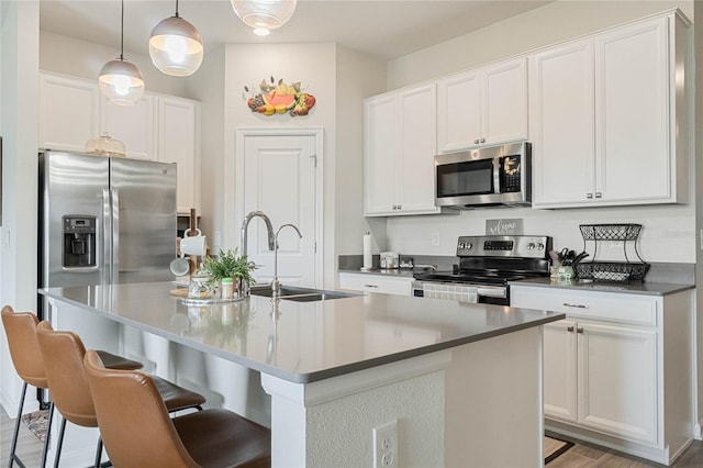 kitchen featuring stainless steel appliances, a sink, a center island with sink, and white cabinets