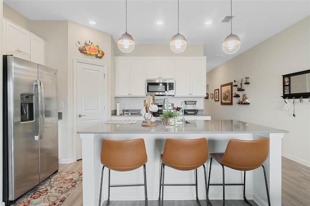 kitchen with a kitchen breakfast bar, stainless steel appliances, visible vents, and white cabinetry