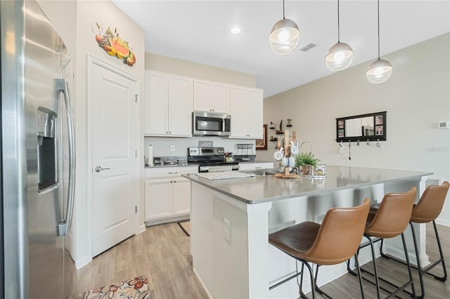 kitchen featuring light wood-type flooring, appliances with stainless steel finishes, a kitchen breakfast bar, and white cabinets