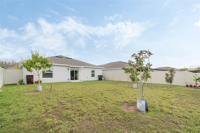 back of house with stucco siding, a fenced backyard, and a yard