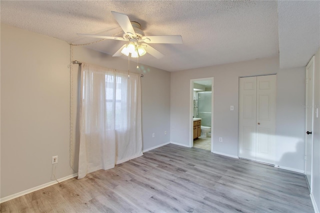 unfurnished bedroom with light wood finished floors, baseboards, a textured ceiling, and ensuite bathroom