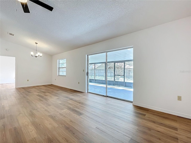 spare room with baseboards, light wood-style flooring, vaulted ceiling, a textured ceiling, and ceiling fan with notable chandelier