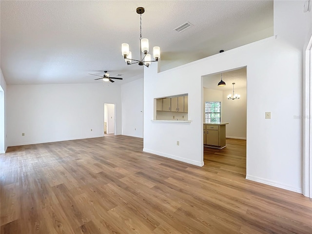 unfurnished living room with visible vents, a textured ceiling, wood finished floors, baseboards, and ceiling fan with notable chandelier