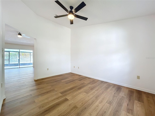 spare room with ceiling fan, a textured ceiling, baseboards, and wood finished floors