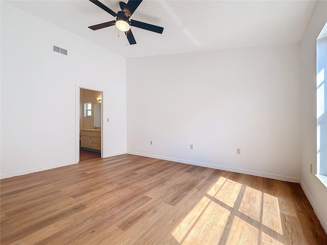 unfurnished room featuring lofted ceiling, visible vents, light wood-style flooring, a ceiling fan, and baseboards