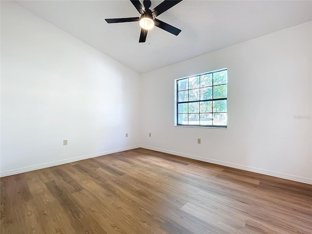 spare room with ceiling fan, vaulted ceiling, baseboards, and wood finished floors