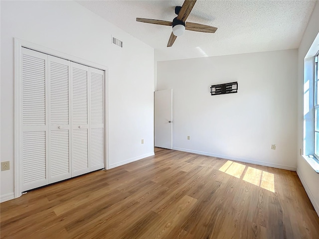 unfurnished bedroom featuring a closet, visible vents, a textured ceiling, and wood finished floors