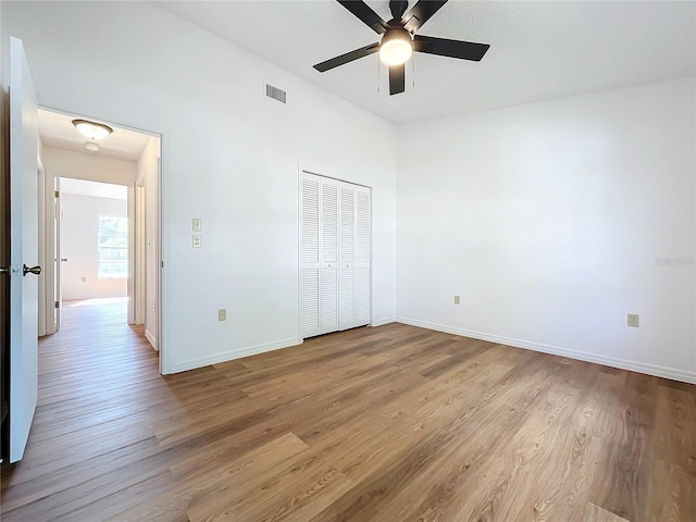 unfurnished bedroom with a closet, visible vents, ceiling fan, wood finished floors, and baseboards