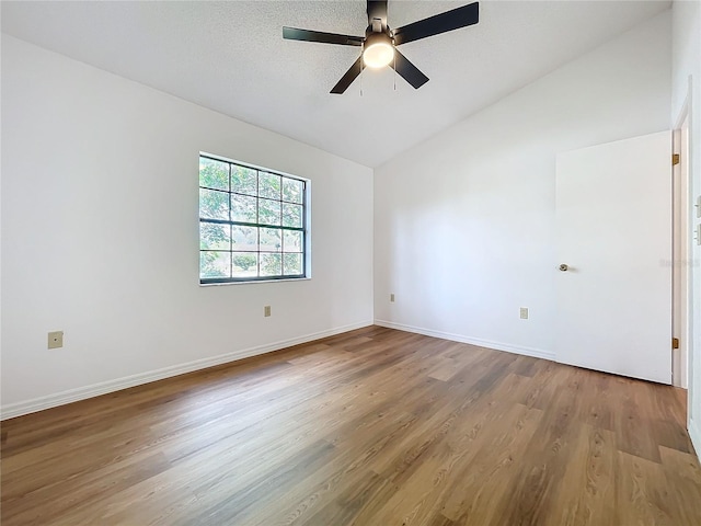 spare room featuring lofted ceiling, a textured ceiling, baseboards, and wood finished floors