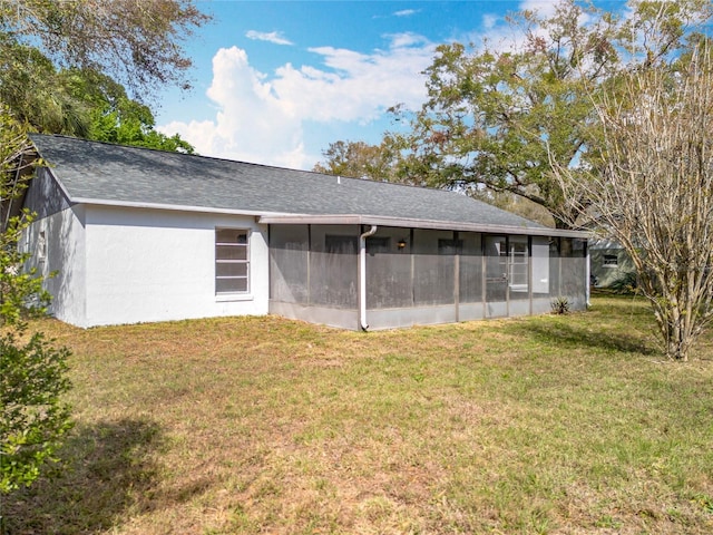 rear view of house with roof with shingles, a lawn, a sunroom, and stucco siding