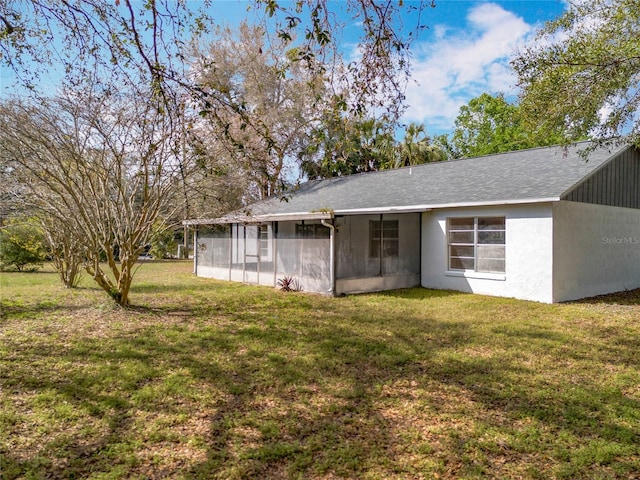 rear view of property featuring a yard, roof with shingles, a sunroom, and stucco siding