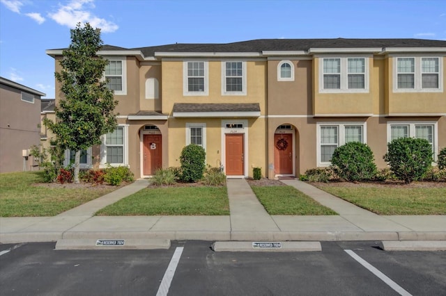 view of property with uncovered parking, a front yard, and stucco siding