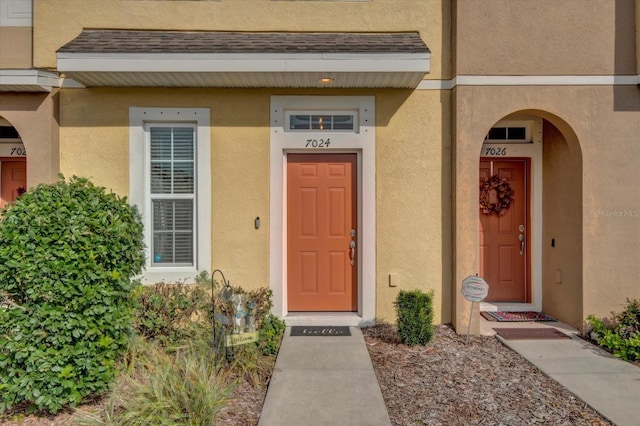 entrance to property featuring a shingled roof and stucco siding