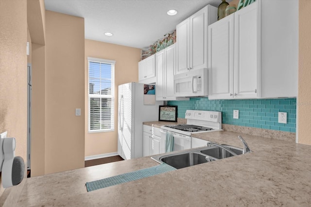 kitchen featuring white appliances, tasteful backsplash, white cabinets, light countertops, and a sink