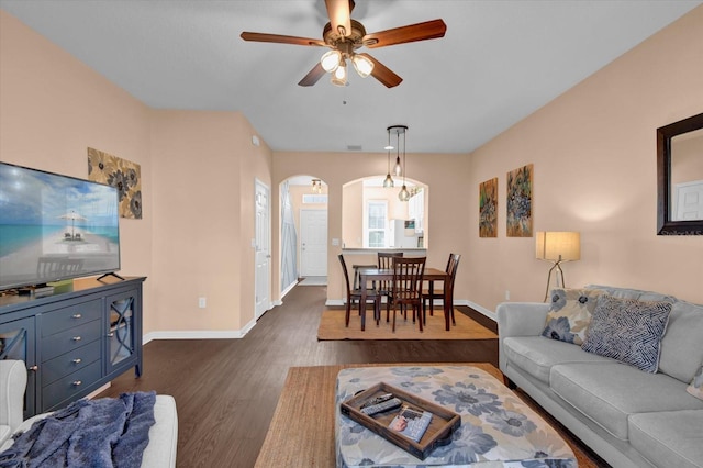 living area featuring arched walkways, ceiling fan, dark wood finished floors, and baseboards