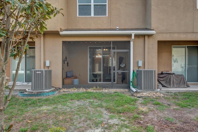 rear view of property featuring a sunroom, central AC unit, and stucco siding