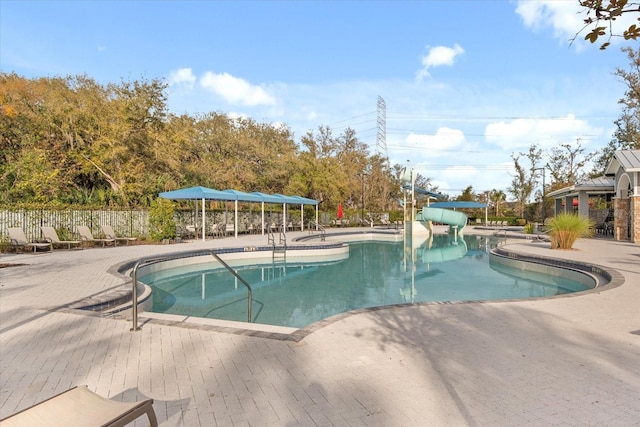 community pool featuring a water slide, a patio area, and fence