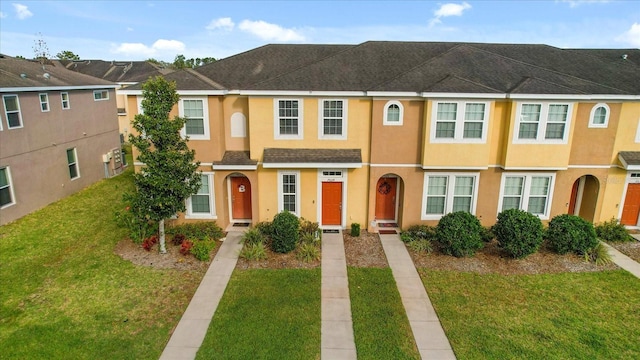 townhome / multi-family property featuring a front lawn, roof with shingles, and stucco siding