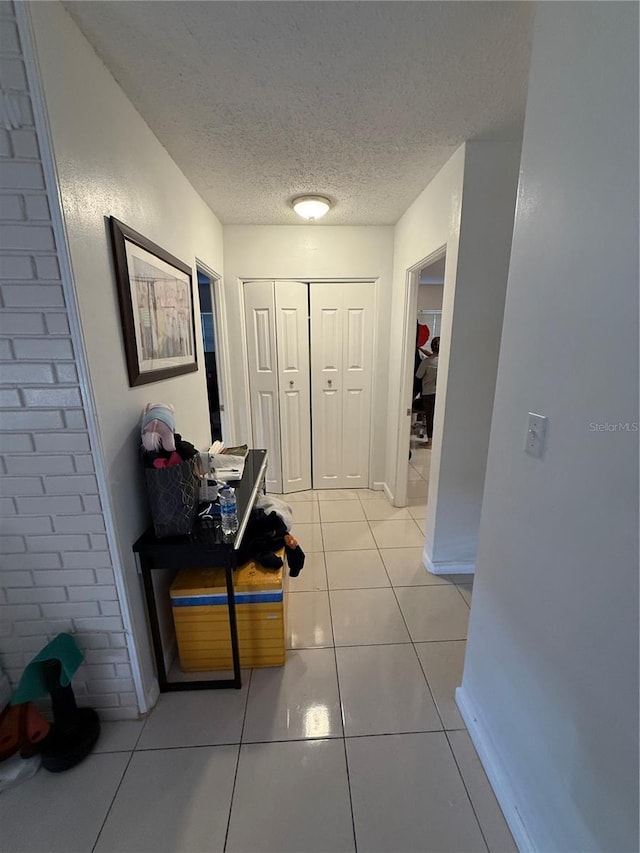 hallway with light tile patterned floors, baseboards, and a textured ceiling