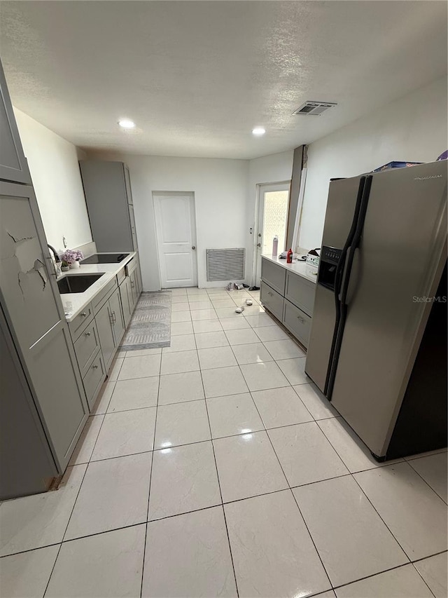 kitchen with light tile patterned flooring, gray cabinetry, a sink, visible vents, and stainless steel fridge with ice dispenser