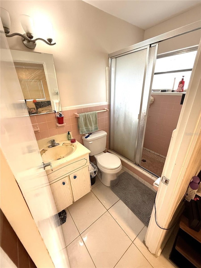 bathroom featuring a stall shower, toilet, tile patterned flooring, vanity, and tile walls